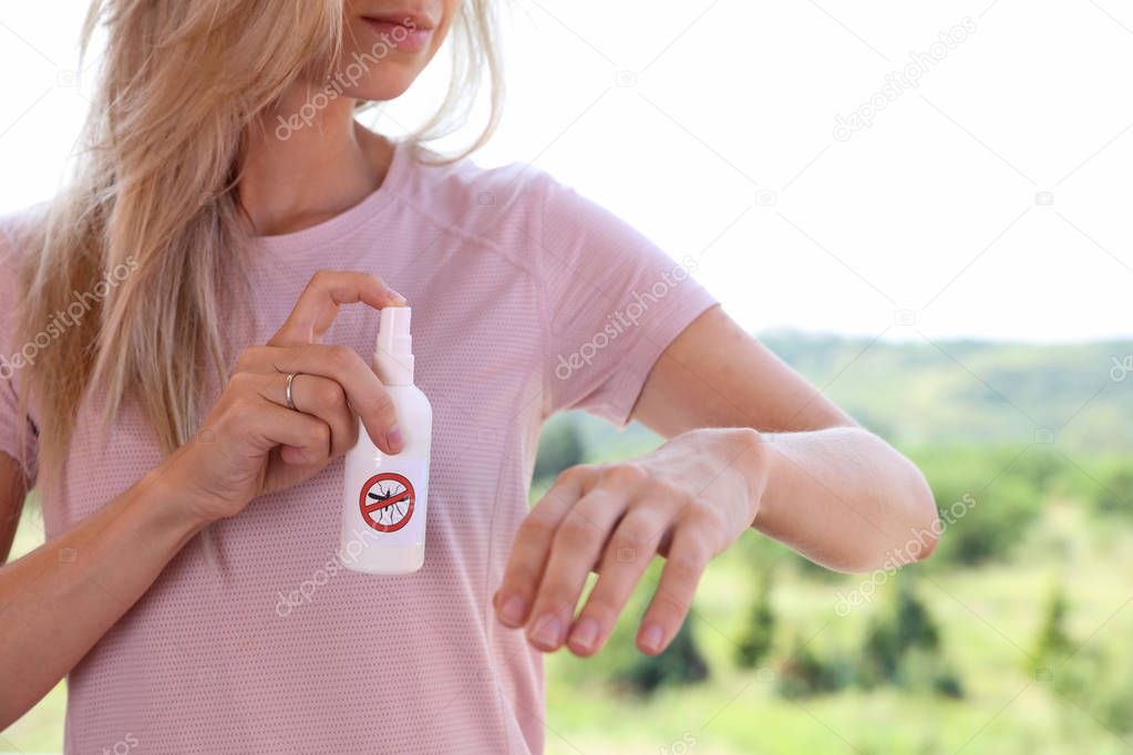 Mosquito repellent. Woman using insect repellent spray outdoors.