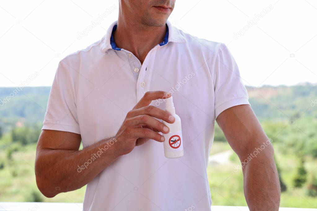 Mosquito repellent. Man using insect repellent spray from bottle outdoors.