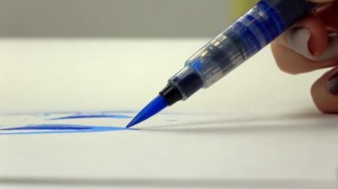 Uyuşuk görüntüleri. Sanatçı kız el bir suluboya fırça mavi mürekkep ile çizer. yakın çekim