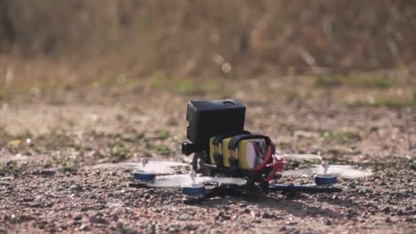 Drone de carreras FPV despega de una superficie de tierra levantando polvo y piedras — Vídeo de stock