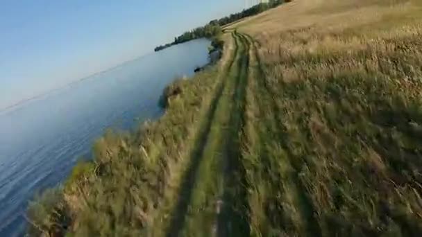 FPV Drone vista de corrida. Voe sobre a costa com campo e estrada de terra — Vídeo de Stock