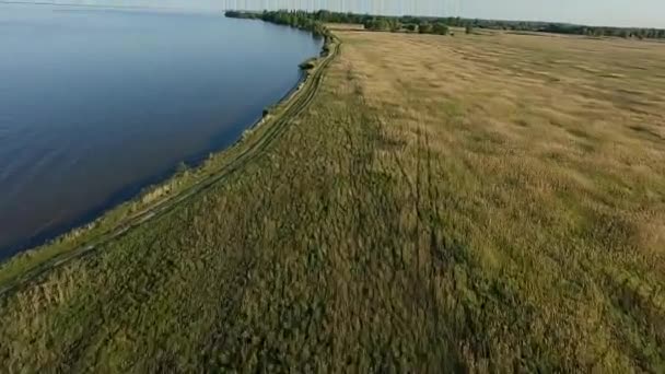 FPV Drone гоночний вид. Політ над береговою лінією з полем і ґрунтовою дорогою — стокове відео