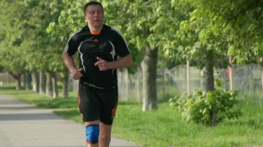 Beyaz erkek koşucu parkta ağaçlarla koşuyor. Yavaş çekim. 7 Temmuz 2020 Kyiv, Ukrayna