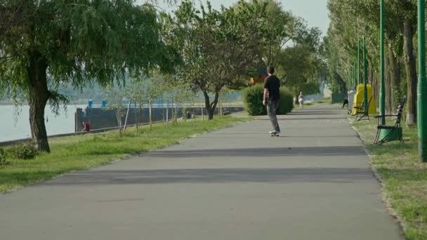 Rapaz patinador a andar na estrada do parque em aterro. Tiro em câmara lenta — Vídeo de Stock