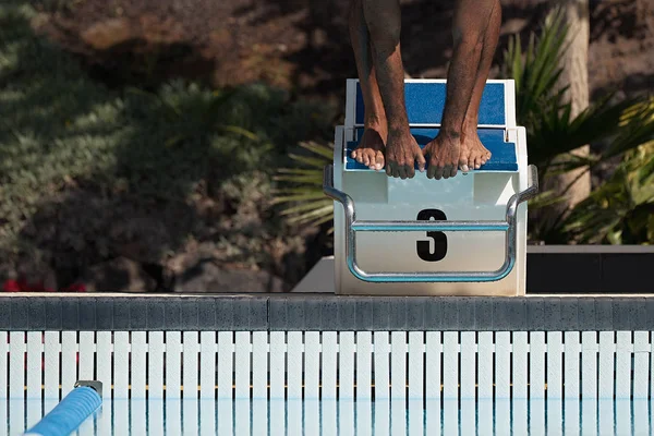 Male swimmer jumps off starting block and start swims in pool
