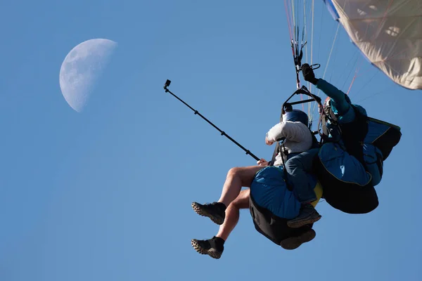 Paraglider tandem fly against the blue sky, tandem paragliding guided by a pilot in the background with the moon