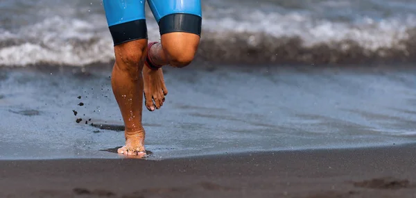 Triathlete swimmer running out of ocean finishing swim race.Fit man ending swimming sprinting determined out of water in professional triathlon suit for ironman