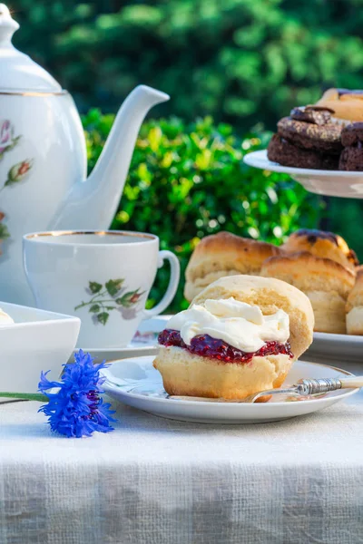 Afternoon tea with cakes and traditional English scones with strawberry jam and clotted cream set up on a table in the garden. Outdoor dining.