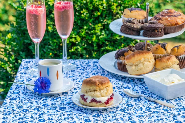 ケーキとアフタヌーン ティーと伝統的な英語スコーンいちごジャムとクロテッド クリームは 庭のテーブルの上を設定しました 屋外での食事 — ストック写真