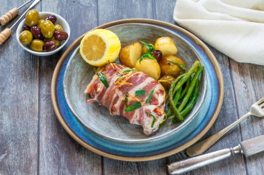 Yüksek açılı görünüş limoni yeni patates, yeşil fasulye ve zeytin - kerevit kuyrukları ile pastırma sarılmış mezgit balığı dolması