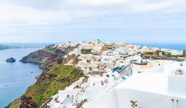 Oia, Yunan adası Santorini bir kıyı kasabası görünümü. Kasaba, engebeli kayalıklara oyulmuş beyaz badanalı evlere sahiptir ve suyla dolu geniş bir kalderaya bakmaktadır..