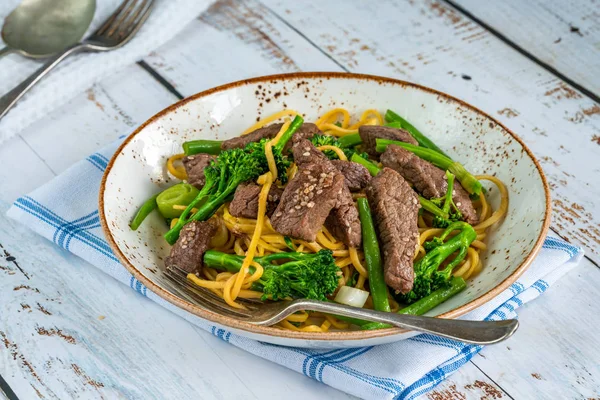 Honey and sesame beef noodles with green vegetables.