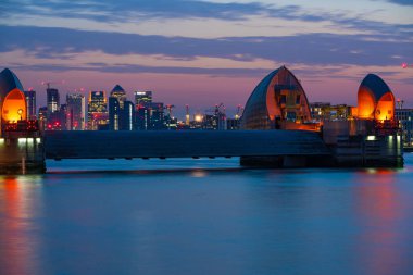 Londra, İngiltere - 29 Haziran 2019: Thames Nehri'nin karşısındaki İngiltere'nin ana finans merkezlerinden biri olan Canary Wharf ve dünyanın en büyük ikinci hareketli sel bariyeri olan Thames Barrier'in gece manzarası