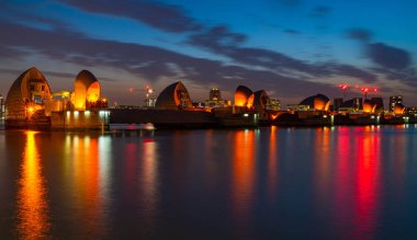 Londra, İngiltere - 29 Haziran 2019: Thames Nehri'nin karşısındaki İngiltere'nin ana finans merkezlerinden biri olan Canary Wharf ve dünyanın en büyük ikinci hareketli sel bariyeri olan Thames Barrier'in gece manzarası