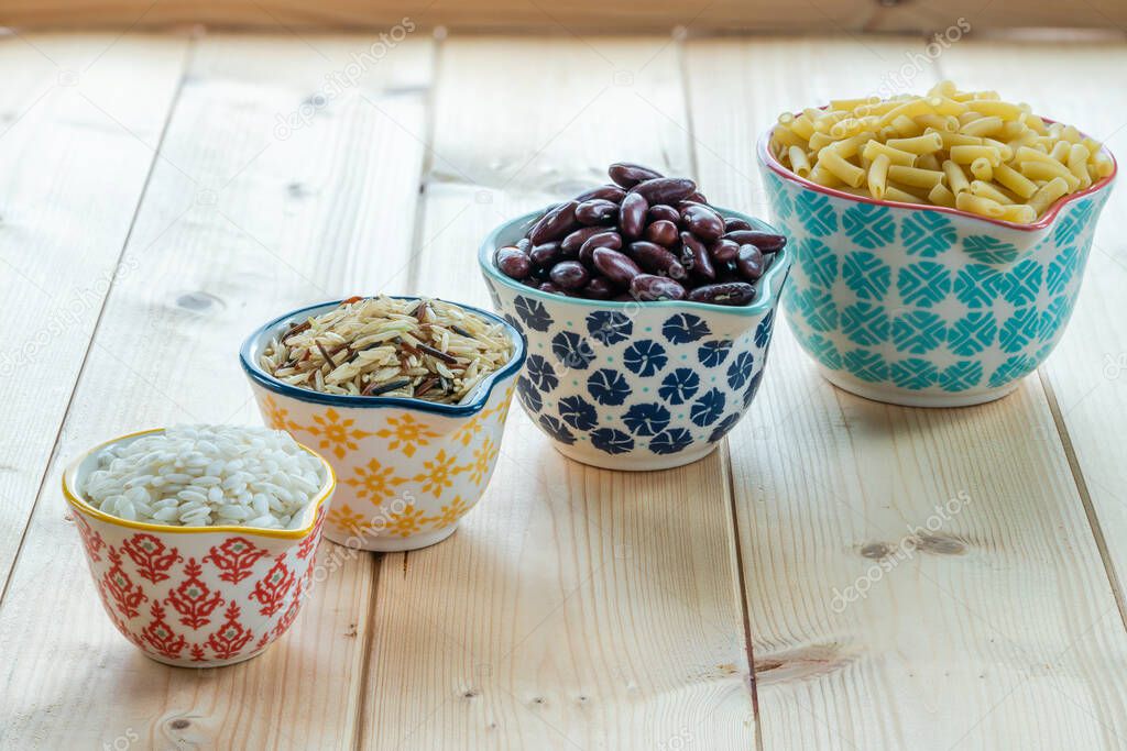 Dry rice, kidney beans and pasta in a ceramic pots on wooden background
