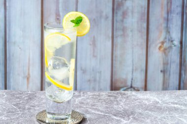 Limonlu ve buzlu su bir dilim limonla süslenmiş ve arka planda nane şekeri - ferahlatıcı soğuk alkolsüz içecek