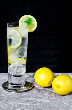 Limonlu ve buzlu su bir dilim limon ve koyu arkaplanda nane ile süslenir. Soğuk, alkolsüz bir içecek.