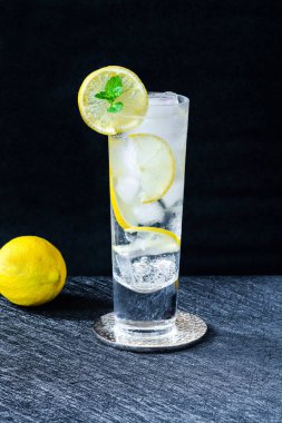 Limonlu ve buzlu su bir dilim limon ve koyu arkaplanda nane ile süslenir. Soğuk, alkolsüz bir içecek.
