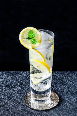 Limonlu ve buzlu su bir dilim limon ve koyu arkaplanda nane ile süslenir. Soğuk, alkolsüz bir içecek.