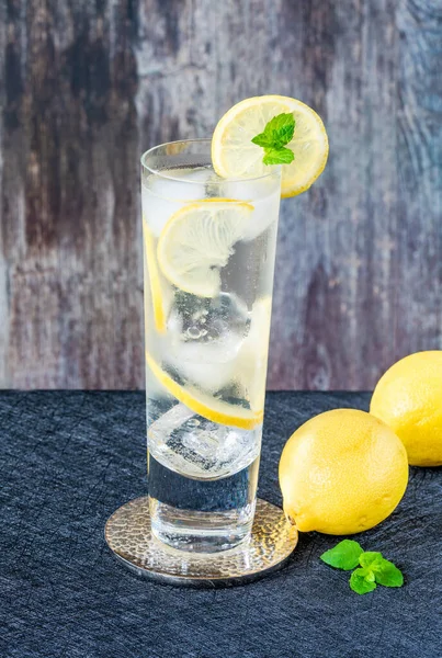 レモンと氷のキューブの水は素朴な背景にレモンとミントのスライスで飾られています さわやかな冷たい非アルコール飲料 — ストック写真