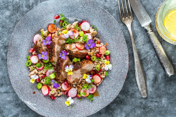 Çıtır ördek, hecelenmiş ve nar salatası, keman çiçekleri ile süslenmiş.