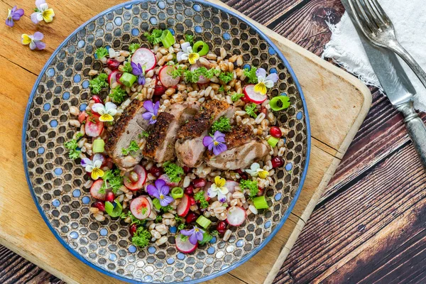 Çıtır ördek, hecelenmiş ve nar salatası, keman çiçekleri ile süslenmiş.