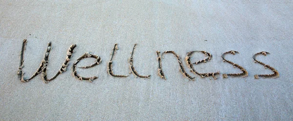 Word Wellness escrito en la arena cerca del mar . —  Fotos de Stock