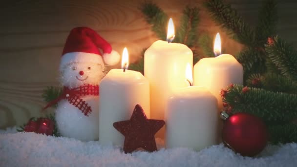 Čtyři hořící adventní svíčky a sněhulák s červeným vánoční ozdoby.