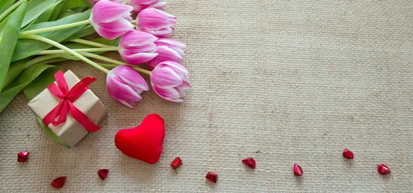 Tulpen und rotes Herz auf braunem Stoff Hintergrund. — Stockfoto