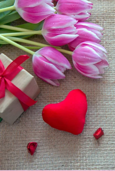Tulpen und rotes Herz auf braunem Stoff Hintergrund. — Stockfoto