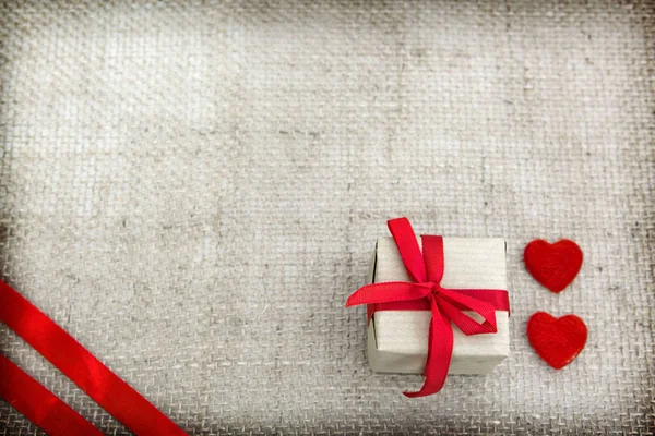 Dwa serca i prezent wyizolowany na brązowym tle tkaniny. — Zdjęcie stockowe