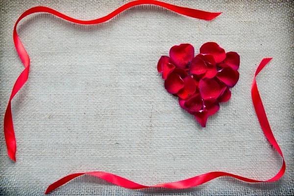 Corazón rojo de pétalos de rosas y lazo aislado sobre un fondo de tela . —  Fotos de Stock