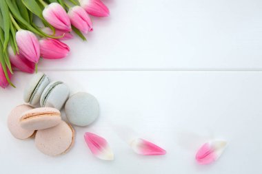 Beyaz arka planda pembe laleler ve makarna kurabiyeleri.