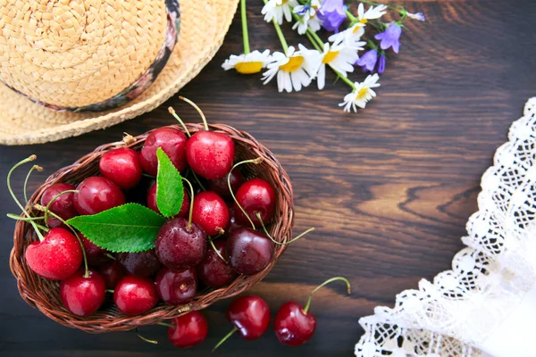 Rote Kirschen und Sommer-Strohhut auf braunem Holztisch. — Stockfoto