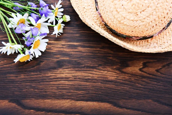 Letní květiny se slámou sluneční klobouk na hnědém dřevěném pozadí. — Stock fotografie