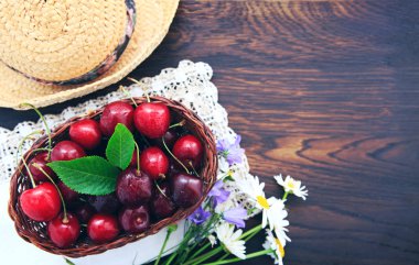 Kahverengi ahşap masa üzerinde Kırmızı Kiraz ve yaz hasır şapka.