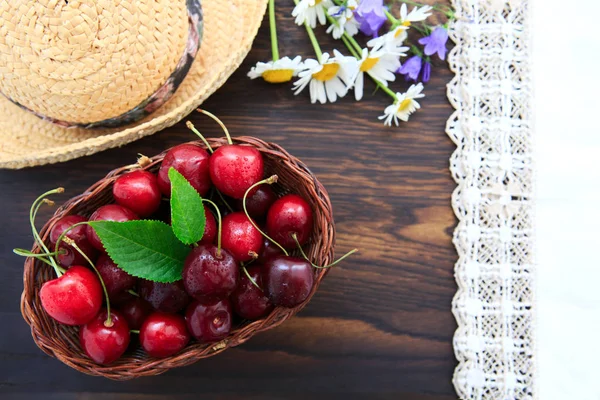 Rote Kirschen und Sommer-Strohhut auf braunem Holztisch. — Stockfoto