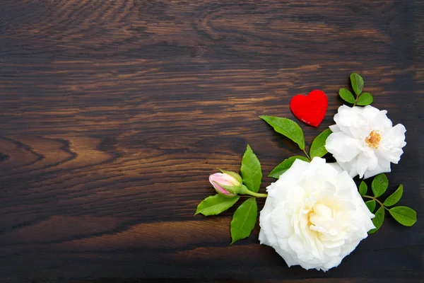 茶色の木製の背景に白いバラと赤い愛の心。スペースのコピー — ストック写真