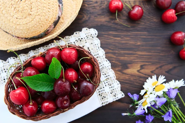 Rote Kirschen und Sommer-Strohhut auf braunem Holztisch. — Stockfoto