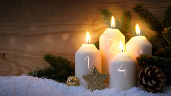 Four burning Advent candles with golden decoration and white snow.