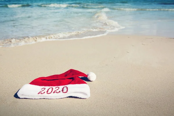 Anno 2020 scritto al cappello di Babbo Natale sulla spiaggia caraibica. Anno nuovo sfondo — Foto Stock