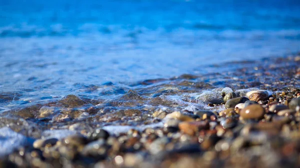 Golven wassen over kiezelstrand, macro shot. — Stockfoto