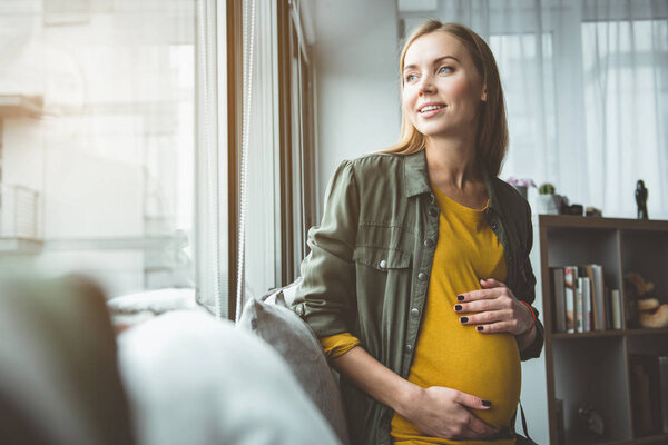 Мечтательная будущая мать сидит на подоконнике
 