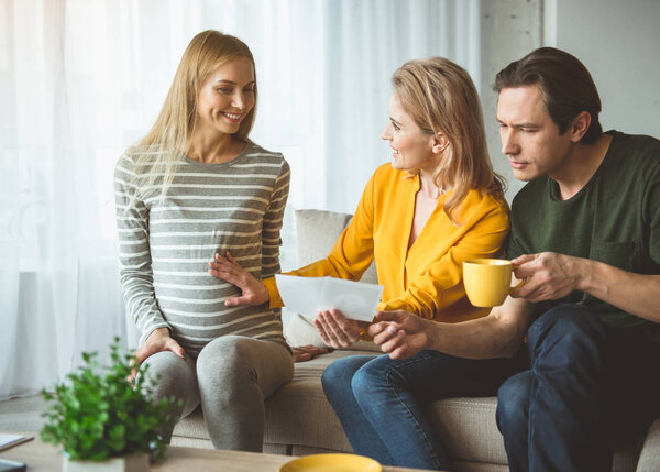 Веселая супружеская пара разговаривает со суррогатной беременной матерью
 