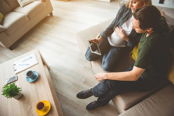 Щасливий чоловік і вагітна жінка використовують планшет в квартирі — стокове фото