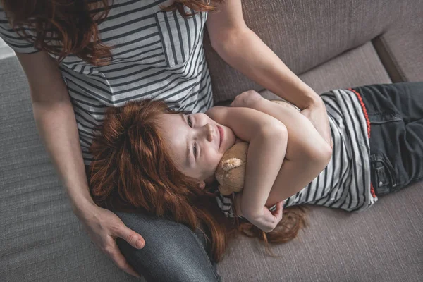 Liten flicka kramar nallebjörn på hennes mor knä — Stockfoto