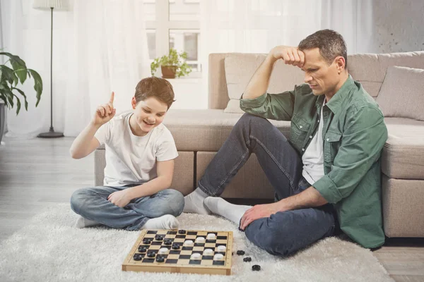 Filho alegre ganhando seu pai em jogo intelectual — Fotografia de Stock