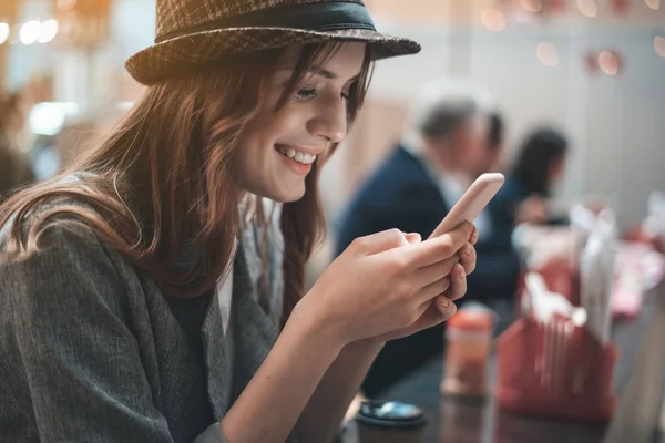 Ухмыляющаяся женщина использует смартфон в кафе — стоковое фото