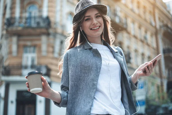 Радостная юная леди с мобильными устройствами и горячим напитком на улице — стоковое фото