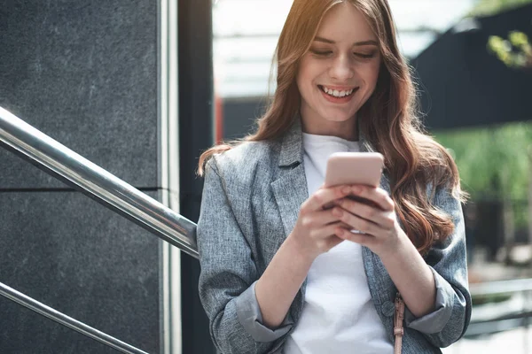 Mujer joven sonriente mirando su teléfono cerca de las barandillas — Foto de Stock